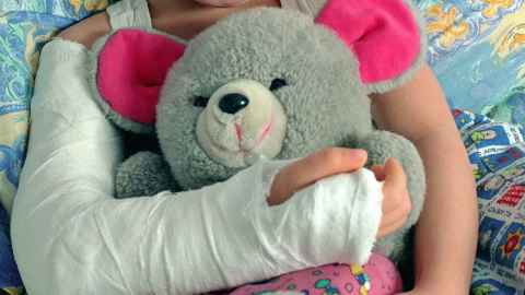 A child with an arm in a cast, holding a teddy bear.