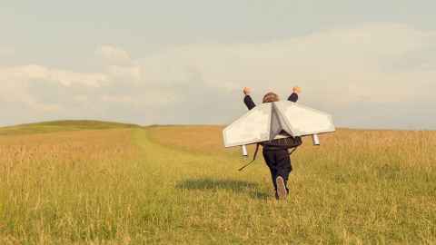 A young boy is pictured "thinking big" with carboard jet wings attached to his back as he runs up a hill: In post-normal times we need creativity and imagination, says Peter O'Connor. Photo iStock