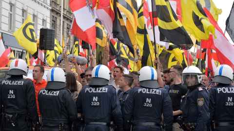 A crowd of people with flags and a line of police in uniforms with 'Polizei' on the back.