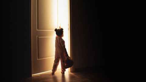 A little girl in shadow, opening a door.