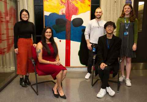 Malvindar with students Adelie Tan (PhD student), Ieuan Sargent (Biomed Hons), Florence Layburn (Biomed Hons) and Henry Liu (Biomed Hons). hey are sitting in front of one of artist Pat Hanly's 'The Seven Ages of Man' works. 