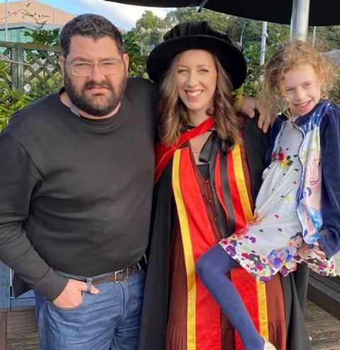 A woman in graduation regalia with a man and a little girl.