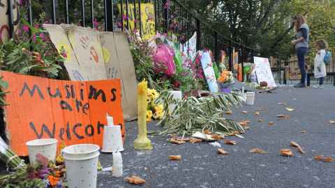 Flowers, candles and a sign that reads 'Muslims are welcome' by a wrought iron fence.