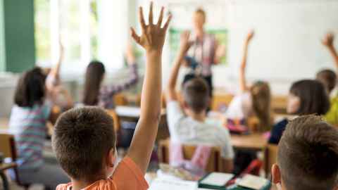 Primary school pupils raising their hands in a classroom.
