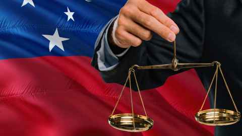 A person holding scales in front of a Samoan flag.