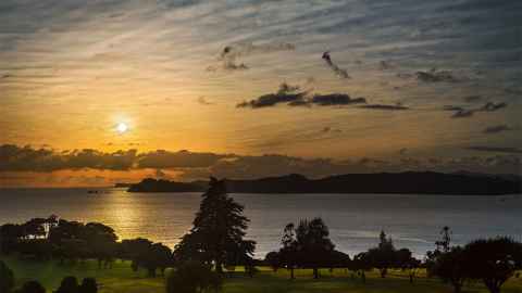 The sun rising over a grassy area by a harbour.