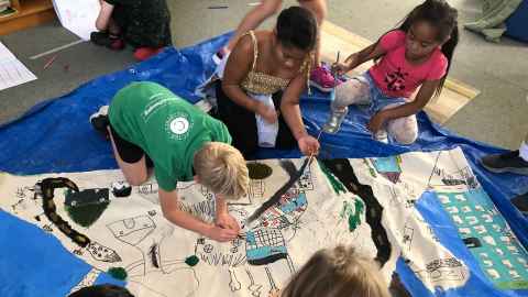 Children painting a canvas on the floor.