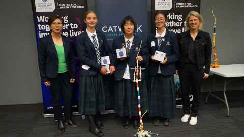 Three schoolgirls in uniform, between two smiling women.