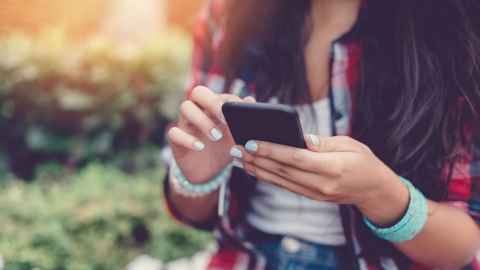 A young woman with painted fingernails looking at a smartphone.