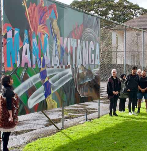 The colourful mural on a wire fence with people gathered around.
