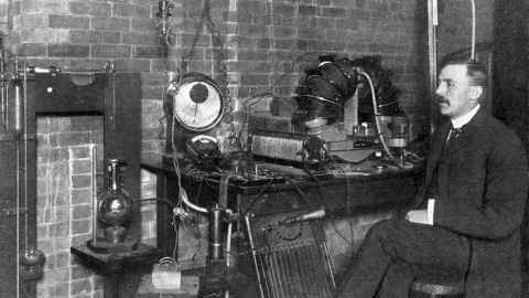 A black-and-white photo of a man sitting at a machine.