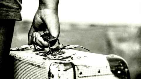 A hand holding a suitcase, in black and white.