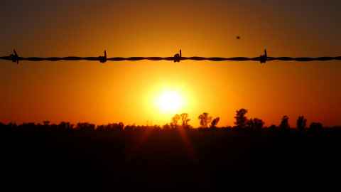 The sun setting behind a line of barbed wire.