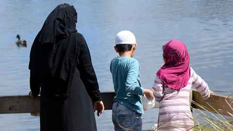 A woman in a hijab with two children, looking at ducks on water.