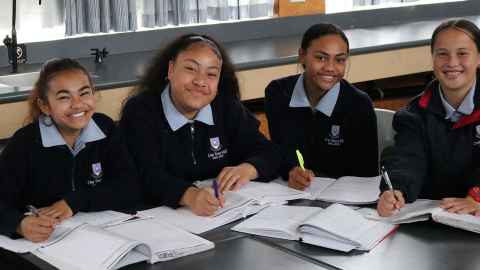 Four secondary school girls in uniform, smiling.