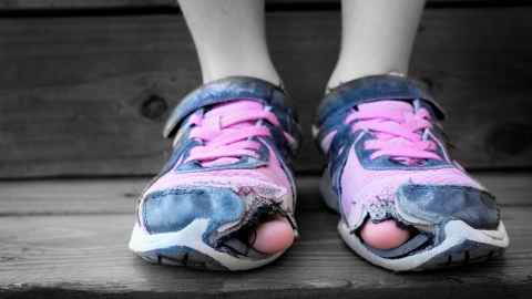 A child's toes poking through sneakers with holes in them.
