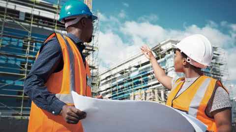 A man and woman in high-vis and hard hats at a construction site.
