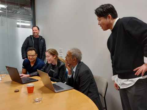 Five people in a small room, looking at two laptops.