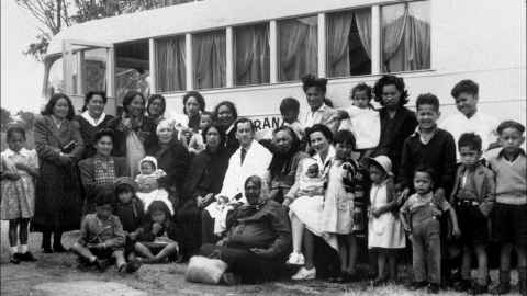 A black and white photo of a large group of people in front of a bus.