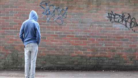 A person in a hoodie looking at a brick wall with graffiti.