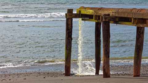 Discharge from a pipe flowing on to a beach, at the water's edge.