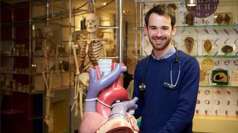 Cameron Wells, with anatomical models, skeletons and tissue samples in the background.