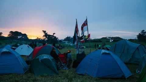 Tents pitched on a green field with Māori flags flying.