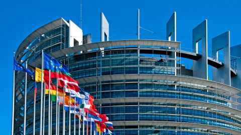 A round, modern building with many flags flying outside, including the EU flag at the front.