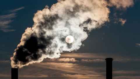 Smoke from industrial chimneys covers the full moon.