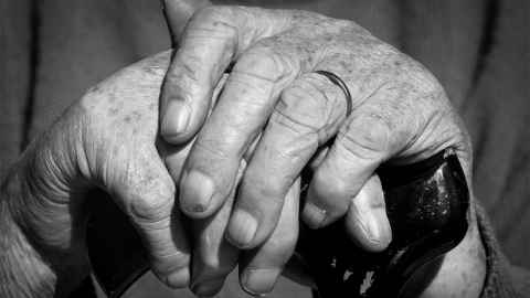 An elderly person's hands, resting on a walking stick.