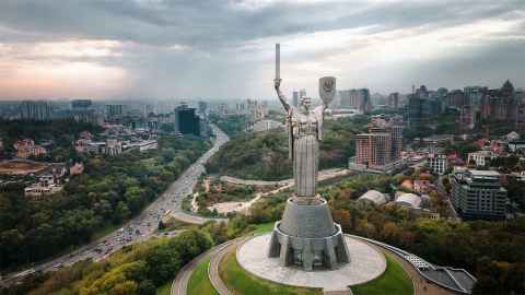 A huge statue of a woman holding a sword and shield, with a large city in the background.