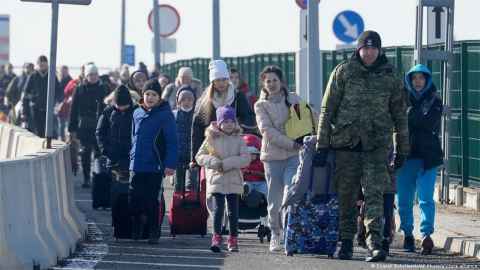 A group of people in winter coats walking, wheeling suitcases behind them.
