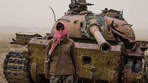 A figure wrapped in a pink headscarf in front of an army tank.
