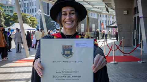 A smiling woman holding up her PhD diploma.