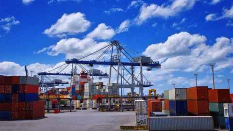 A busy port with cranes and containers, on a fine day.