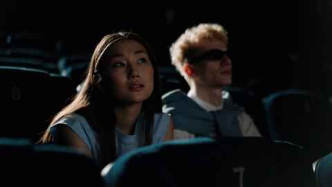 An Asian woman leaning forward in a cinema seat, with a European man sitting beside her.