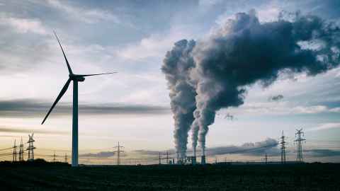 A wind turbine near industrial chimneys belching dark grey smoke.