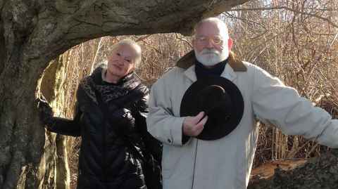 A woman and man in winter coats, with trees in the background stripped of leaves.