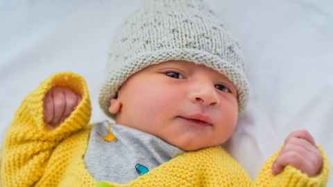A baby wearing a yellow cardigan and a knitted hat.