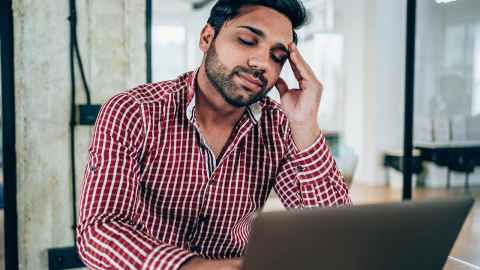 A man looking at a laptop with a hand on his head.