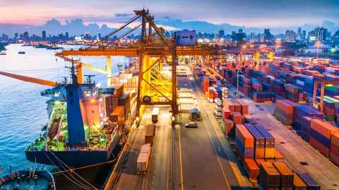 A busy urban port, with container ships docked and in the process of being unloaded.