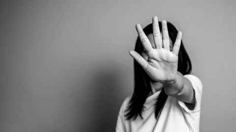 A woman holding a hand up to the camera, covering her face, in black and white.