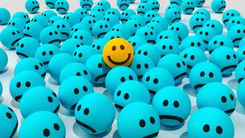 A group of turquoise balls with sad faces on them, and one yellow happy face ball in the middle.