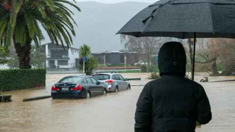 A shadowy figure with an umbrella, looking out on a flooded street.