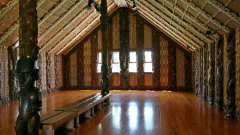 The intricately decorated interior of a Māori meeting house, with traditional carvings and woven panels.