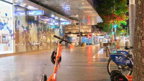 Orange scooters and bikes on the footpath of a deserted street at night.