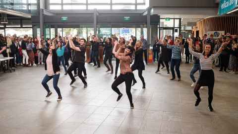 A group of about a dozen people dancing, surrounded by onlookers.