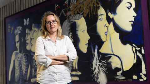 Monika Byrne in front of mural showing women's heads. 