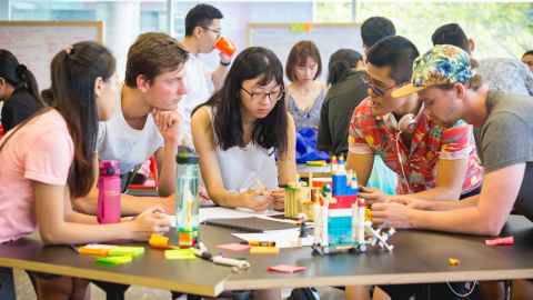 A group of young people sitting around a table with Lego models on it