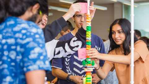 A group of people building a tower of Lego